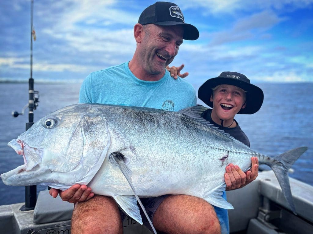 A father and son smile while proudly holding the giant trevally that they caught on a fishing trip with Mentawai Fishing at Villa Onu