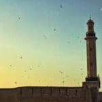 Eid al-Fitr, a mosque tower with the sunset backdrop and the new crescent moon visible.